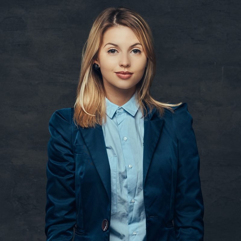 Portrait of a sensual blonde business woman dressed in a formal suit and blue shirt. Isolated on a dark background.